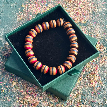 Handmade bracelet made from rounded recycled skateboard beads in pink, blue and black tones, presented in a green gift box.