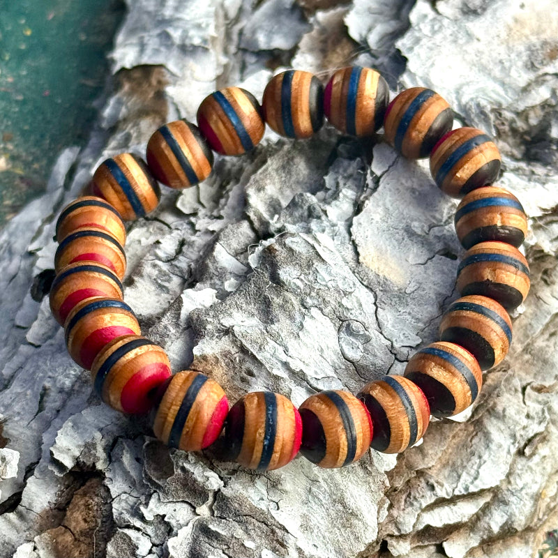 Bracelet made from recycled skateboard wood with blue, pink, and black colour tones, shown on textured bark with rounded handcrafted beads.