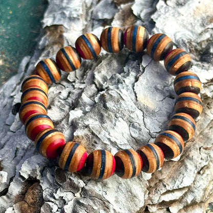 Bracelet made from recycled skateboard wood with blue, pink, and black colour tones, shown on textured bark with rounded handcrafted beads.