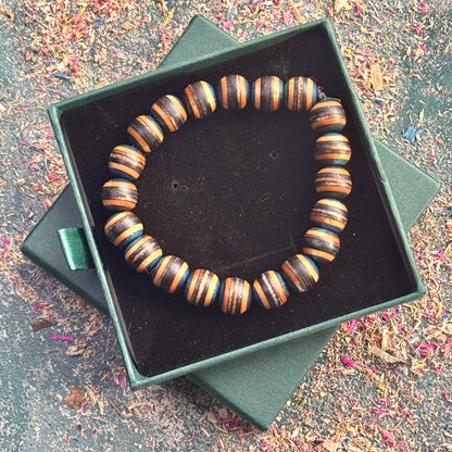Handmade bracelet crafted from recycled skateboard wood beads arranged in alternating brown, black and blue colour tones, displayed in an open green gift box on a textured background.