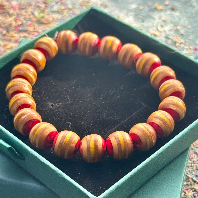 Close-up of a beaded bracelet made from recycled skateboard wood, showing yellow and orange tones with red accents on a gift box background.