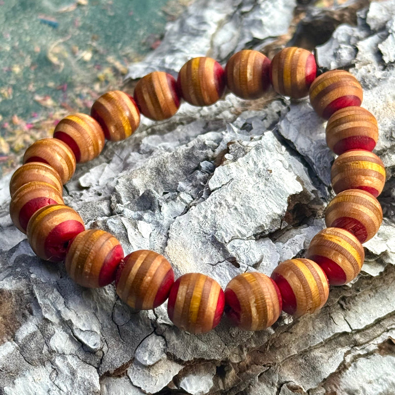 Bracelet made from recycled skateboard wood with rounded beads in red and yellow tones, shown on a textured surface.