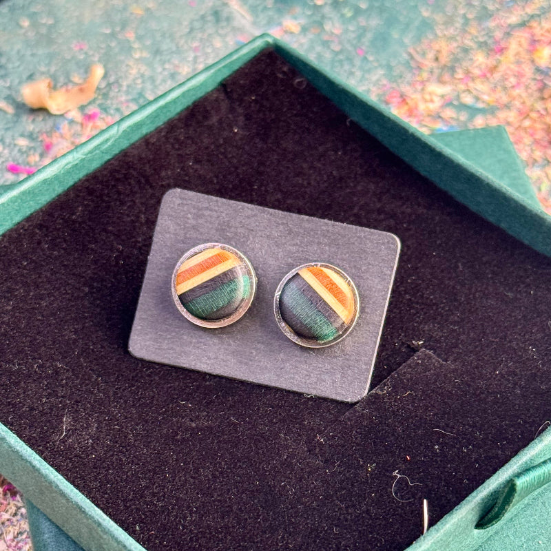 Stud earrings made from recycled skateboard wood with green and black tones, shown on a backing card inside a green gift box.