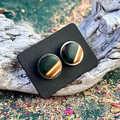 Stud earrings made from recycled skateboard wood with green and black tones, shown on a black card against driftwood.