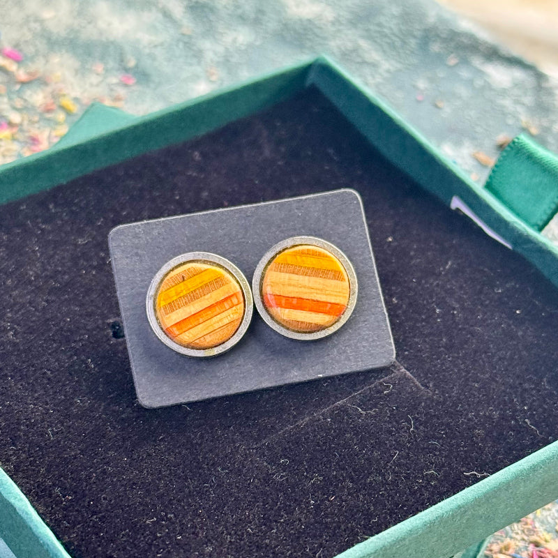 Pair of yellow and orange striped skateboard wood stud earrings shown on a backing card inside a green gift box.