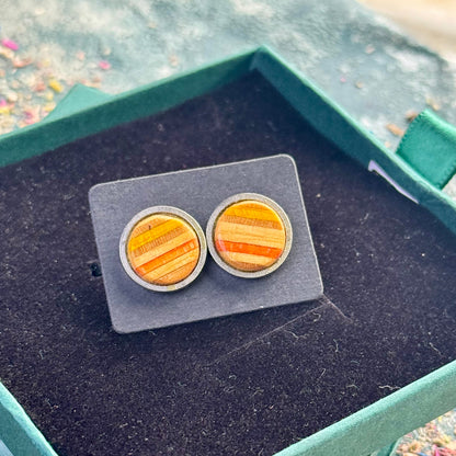 Pair of yellow and orange striped skateboard wood stud earrings shown on a backing card inside a green gift box.