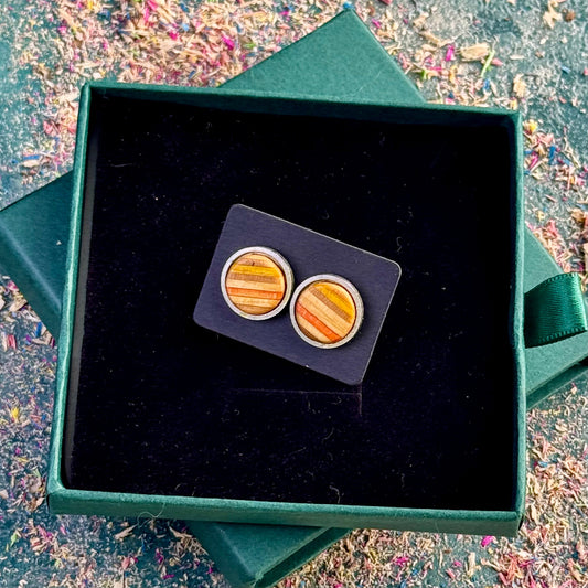 Close-up of yellow and orange striped skateboard wood stud earrings presented on a black backing card inside a dark green gift box.
