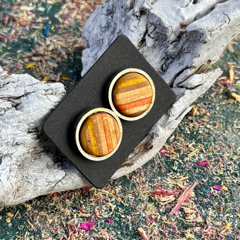 Stud earrings made from recycled skateboard wood, showing yellow and orange tones on a flat-lay card against driftwood.