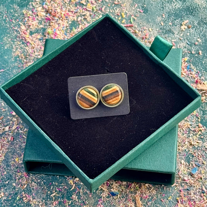 Close-up of stud earrings made from recycled skateboard wood, showing green, black and brown tones on a backing card inside a gift box.