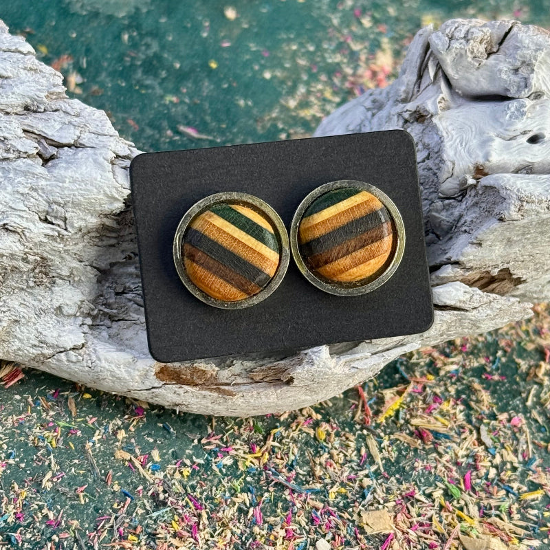 Green, black and brown skateboard wood stud earrings shown close-up on a black card against driftwood and textured background.