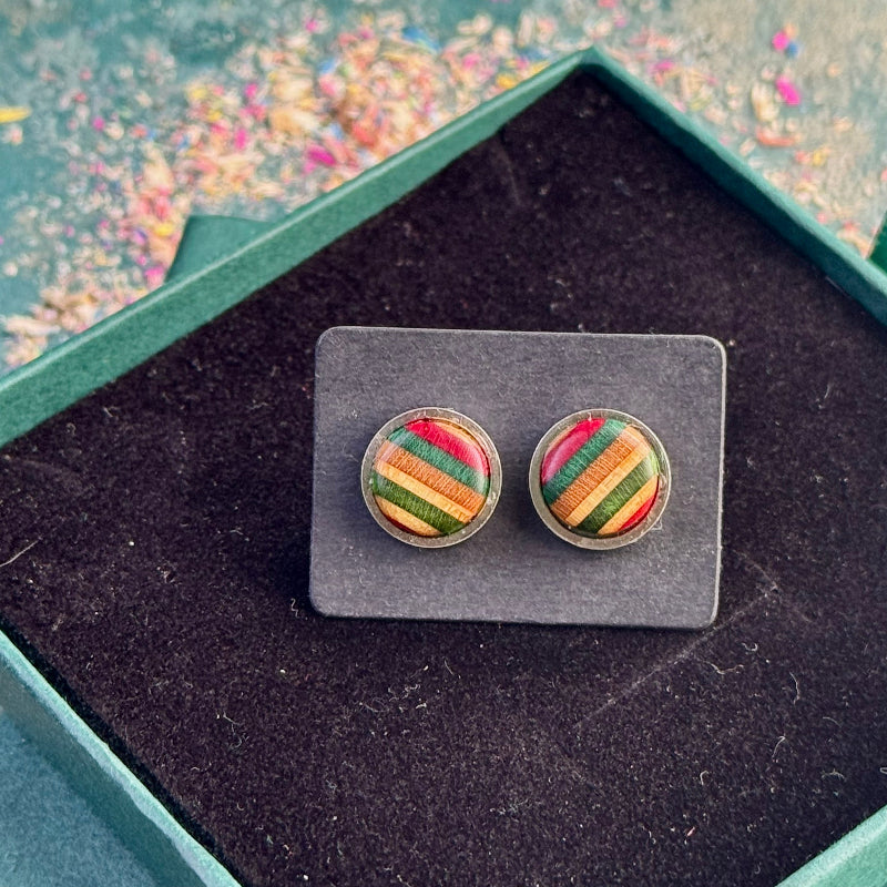 Stud earrings made from recycled skateboard wood, showing red and green striped tones on a backing card inside a gift box.