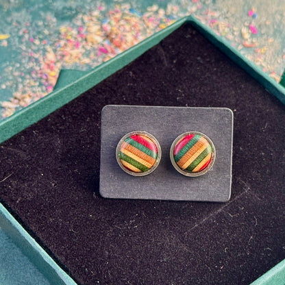 Stud earrings made from recycled skateboard wood, showing red and green striped tones on a backing card inside a gift box.