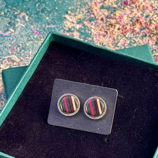 Stud earrings featuring pink, purple, dark green and teal striped skateboard wood, displayed on a dark backing card inside a gift box.