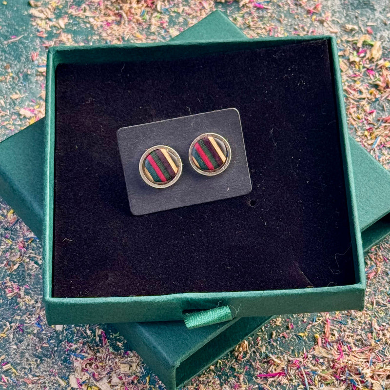Stud earrings with pink, purple, dark green and teal striped skateboard wood shown on a dark card in a gift box.