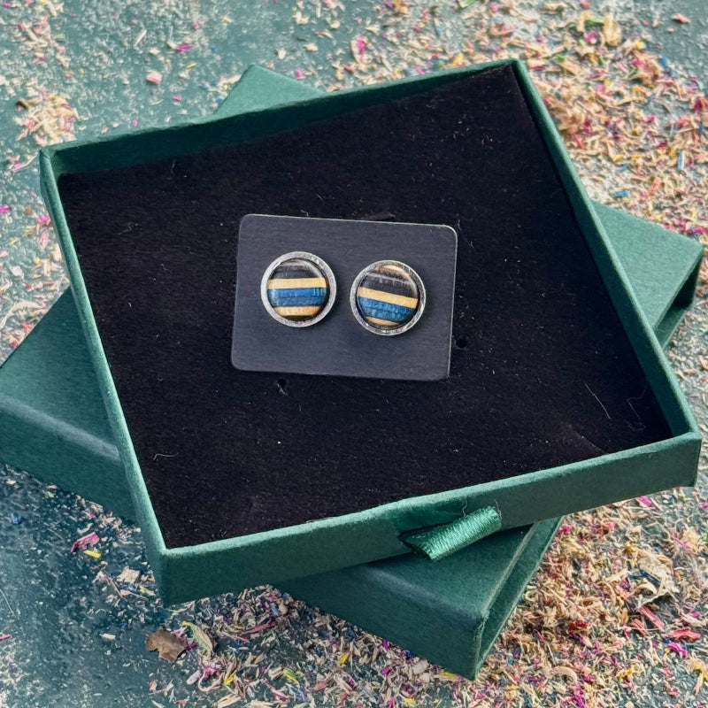 Stud earrings with blue and black striped skateboard wood displayed on a dark card inside an open green gift box.