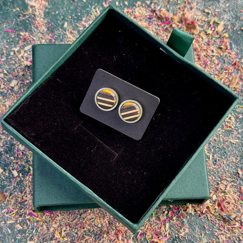 Yellow, white and black striped skateboard wood stud earrings placed on a dark backing card, centred inside an open green gift box.