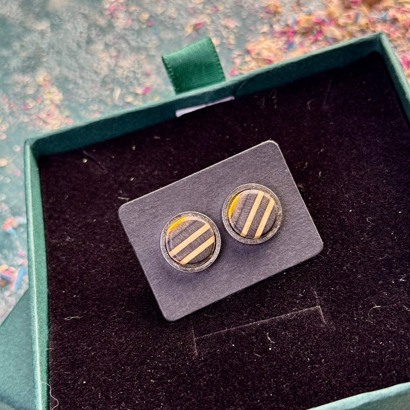 Stud earrings with white, yellow and black striped skateboard wood positioned on a dark card inside an open gift box.