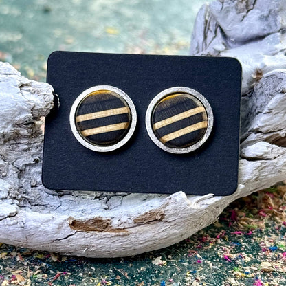 Round stud earrings with black and white striped skateboard wood displayed on a dark card against driftwood.