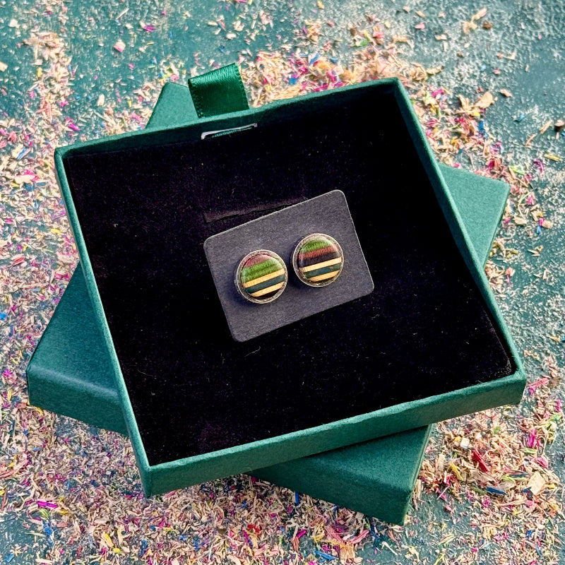 Stud earrings with green, teal and purple striped skateboard wood shown centred in an open gift box on a textured surface.