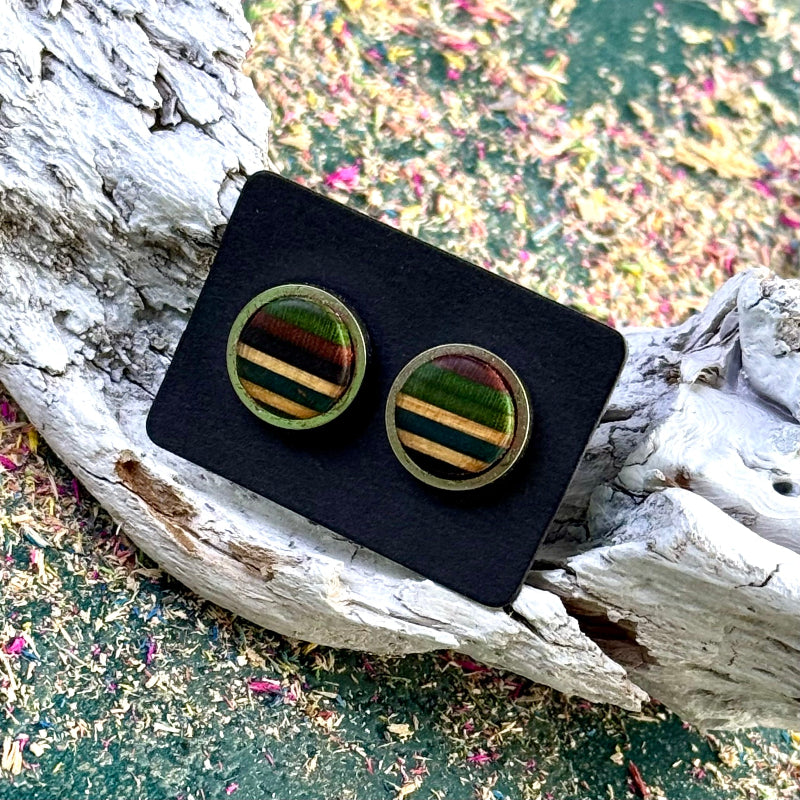 Round stud earrings in green, twal and purple tones displayed on a black card, resting against textured driftwood.