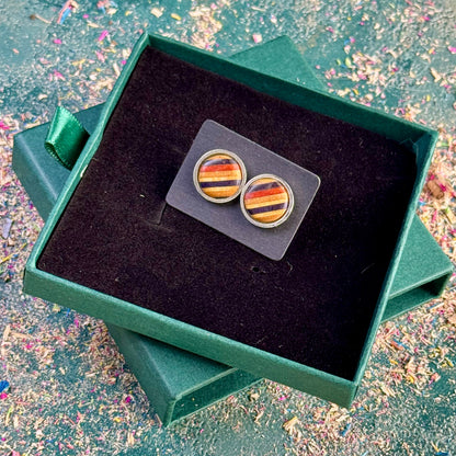 Stud earrings in amber, red and blue tones shown as a flat lay on a dark gift box, crafted from skateboard wood.