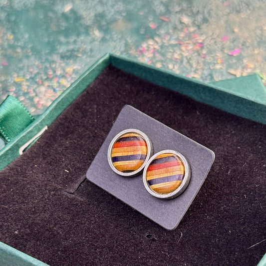 Close-up of stud earrings with amber, red and purple striped skateboard wood resting on a dark display card inside a gift box