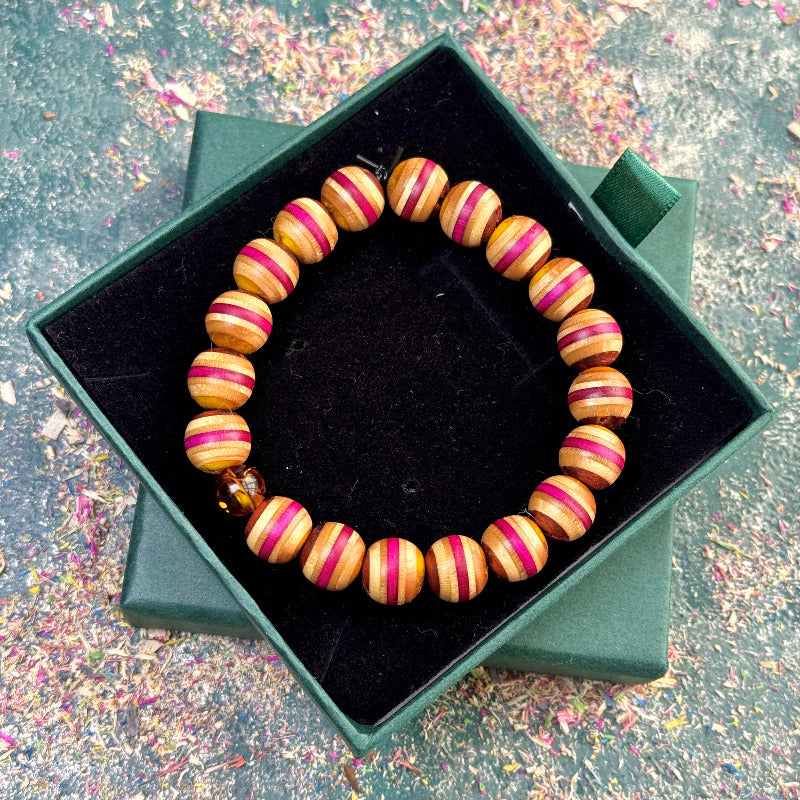 Bracelet made from recycled skateboard beads in yellow, pink, and brown tones, with a single amber bead accent, shown in an open green gift box.