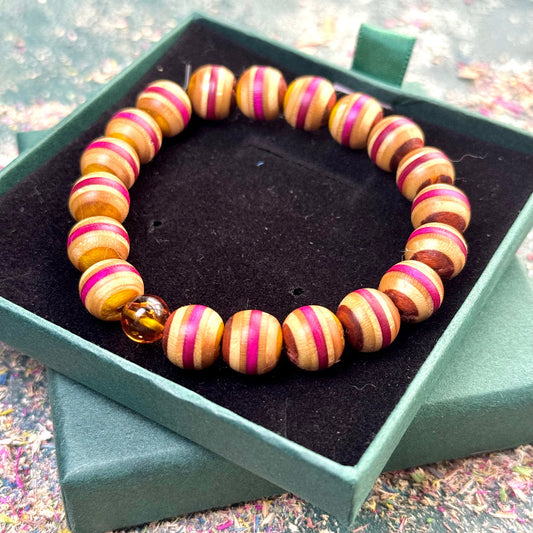 Handmade bracelet with recycled skateboard wood beads in yellow, pink and brown tones, featuring one amber bead, displayed in a green jewellery box.