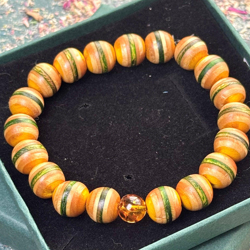 Bracelet made from recycled skateboard wood in green and yellow tones, strung with rounded 10mm beads and finished with one real amber accent bead, displayed in a dark velvet-lined gift box.