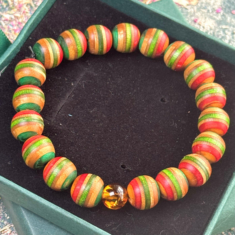 Elastic wooden bracelet made from recycled skateboard beads in green, red, and natural wood tones, finished with smooth oil and completed with a single genuine amber bead resting at the front.