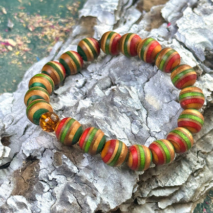 skateboard wood in green, red and natural colour tones, shown on textured bark. One real amber bead features.