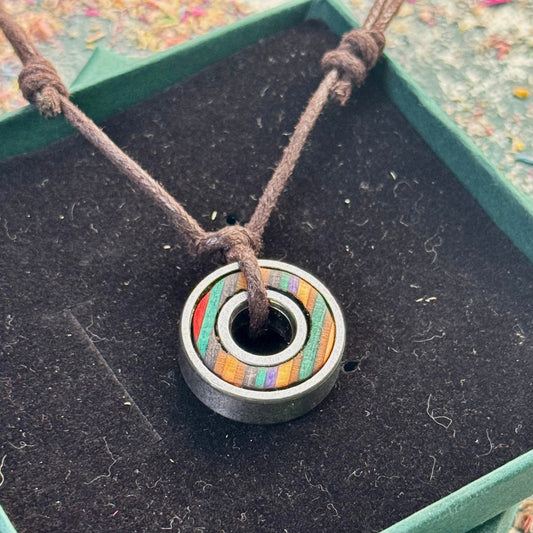 Recycled skateboard ball bearing pendant with turquoise and black colour tones, set inside a steel bearing and hung on a brown adjustable cord, photographed in a green jewellery box.