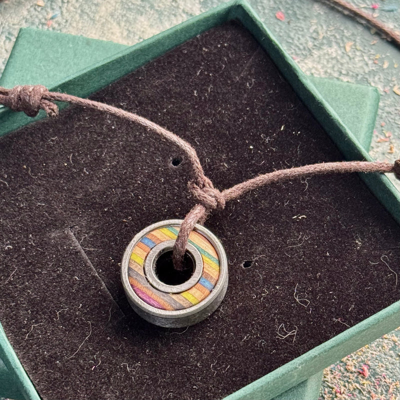 Recycled skateboard bearing pendant in moss green and blue tones on brown adjustable cord, presented in a green gift box.