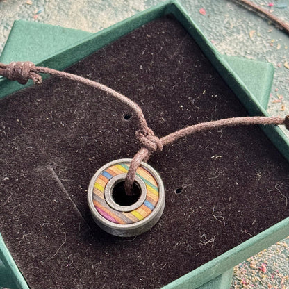 Recycled skateboard bearing pendant in moss green and blue tones on brown adjustable cord, presented in a green gift box.