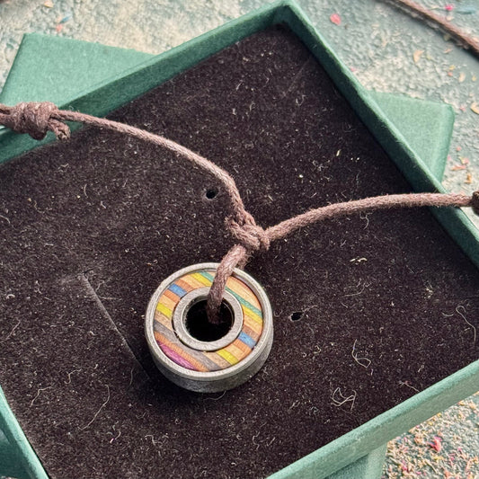 Recycled skateboard bearing pendant in moss green and blue tones on brown adjustable cord, presented in a green gift box.