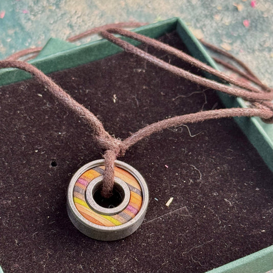  Ball bearing pendant with recycled skateboard wood inlays in purple, black and orange tones, shown on a brown adjustable cord.