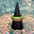 Green, purple and teal recycled skateboard wood ring displayed on a black ring cone, showing layered maple and wood grain.