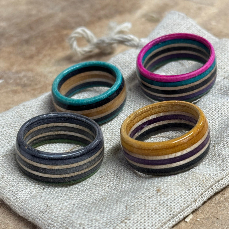 Set of four handmade recycled skateboard rings in various colours, displayed on a rustic linen pouch with natural background.