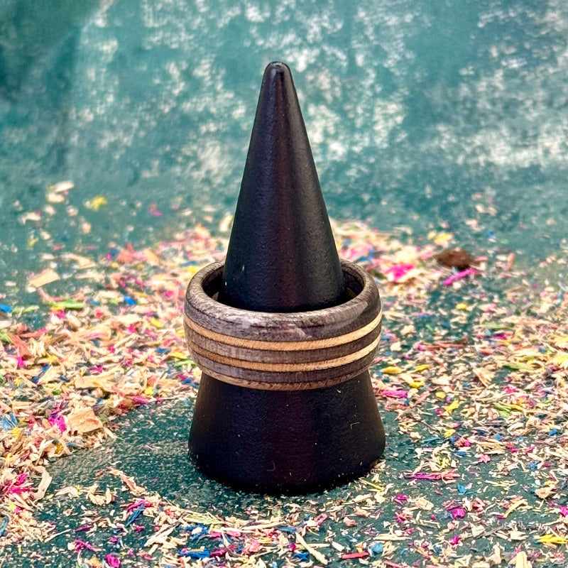 Dark grey recycled skateboard wood ring displayed on a black ring cone, showing layered maple and wood grain.