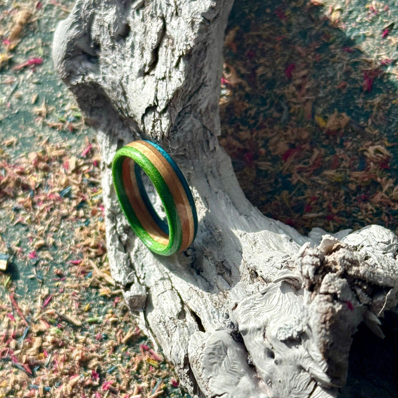 Slim skateboard maple ring with green and blue outer bands, on driftwood.