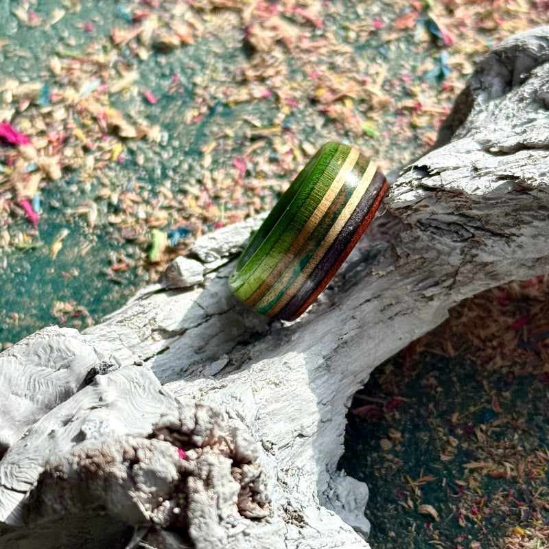 Side view of a green, purple and teal recycled skateboard wood ring resting on weathered wood.