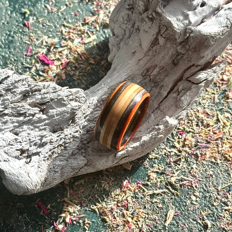 Orange and black skateboard maple ring resting on driftwood, stripes running round the band.