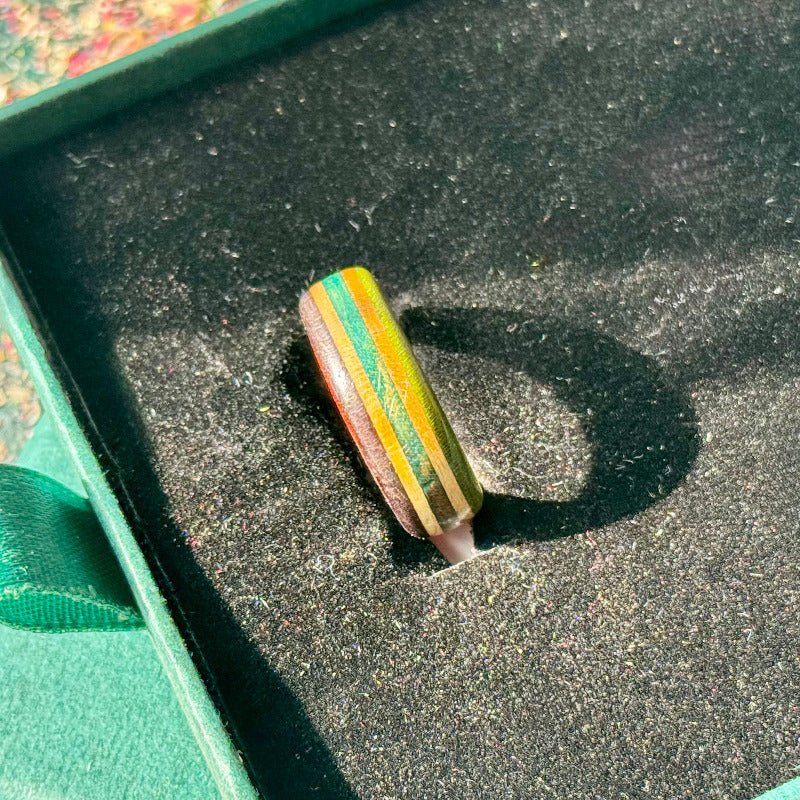Green, purple and teal layers running through a slim skateboard maple band.