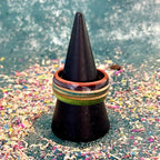 Green, purple and teal recycled skateboard wood ring shown with a second layered skateboard ring on a black ring cone.